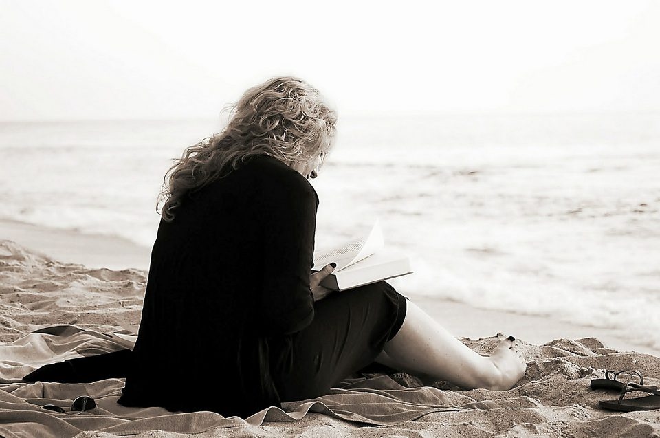 'n Foto van 'n vrou wat bybel lees op 'n strand